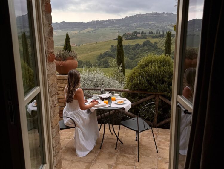 Woman enjoying French toast in Tuscany with a wide view of rolling hills vineyards and countryside from the terrace at Lupaia.